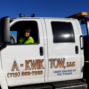 A person in a yellow vest sits confidently in the driver's seat of an "A-Kwik Tow, LLC" tow truck, ready for the next job. With vehicle tracking enhancing their efficiency, the contact details are prominently displayed on the door for easy access.