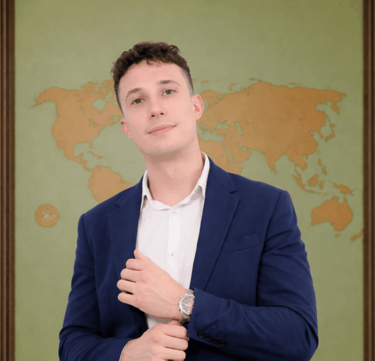A man in a blue suit and white shirt stands in front of a world map background, adjusting his cuff.