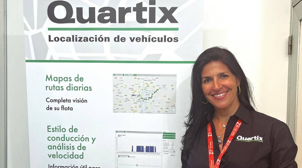 Woman smiling in front of Quartix poster displaying vehicle tracking services, featuring daily route maps and driving style analysis.