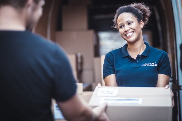 A delivery person hands a package to a recipient in front of a van filled with boxes.