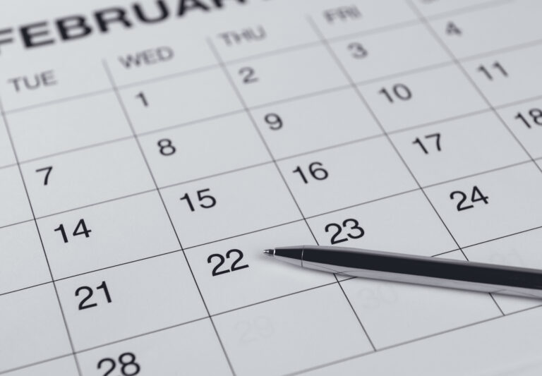 Close-up of a calendar page showing February, highlighting the week of the 21st to 23rd with a pen pointing at the 22nd.