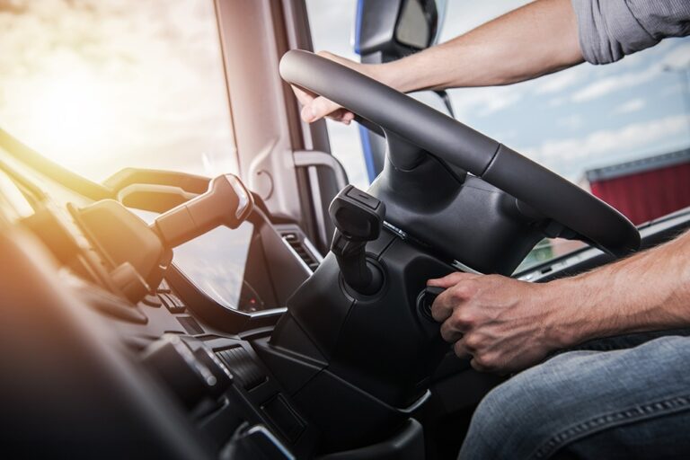 A person is starting a vehicle, hand turning the ignition key as sunlight streams through the window. The steering wheel and dashboard, sleek with modern facilities, are clearly visible.
