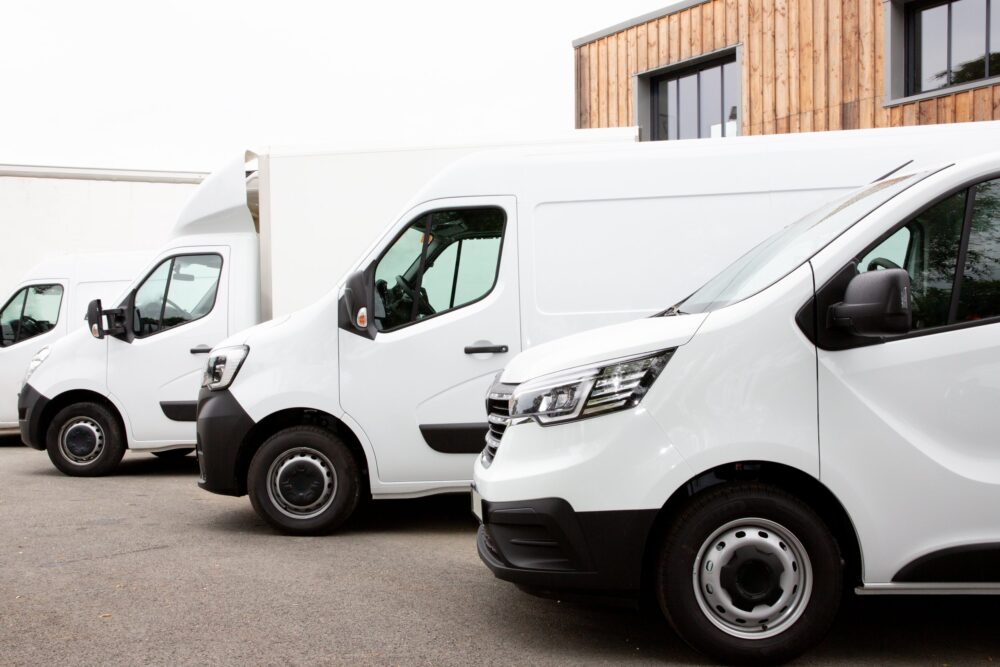 Three white commercial vans are parked side by side in front of a modern wooden building.