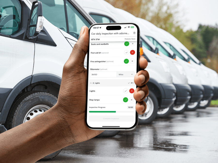 A hand holds a smartphone showing a car inspection checklist app in front of a row of white vans parked outdoors.