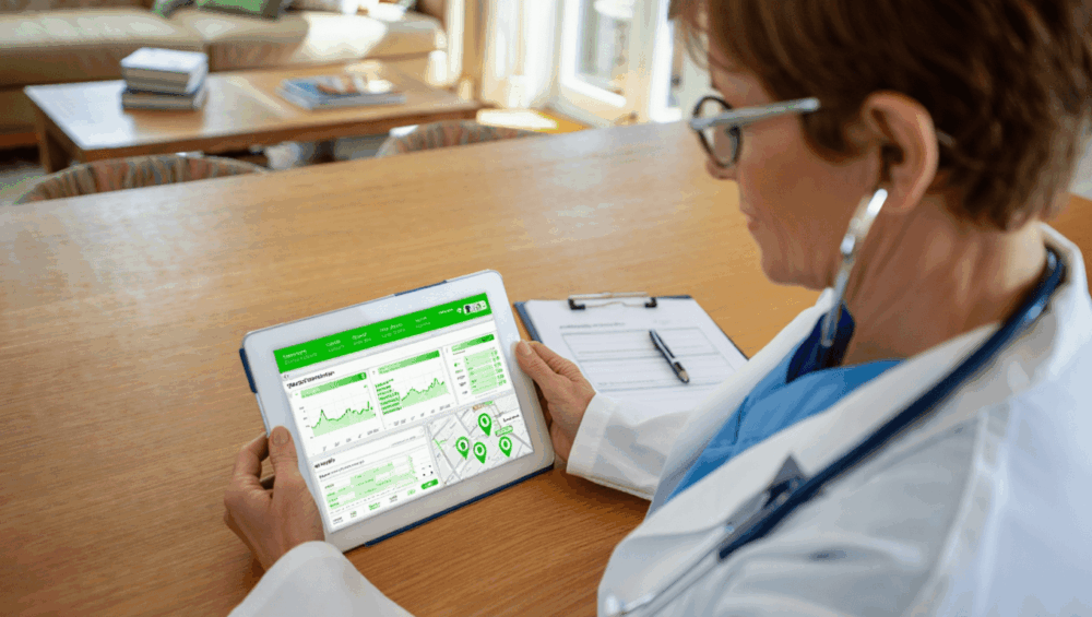 A person wearing a white coat and stethoscope reviews green data charts and maps on a tablet at a wooden table, utilizing Fahrzeugortung für Pflegedienste to optimize routes, with a clipboard nearby.