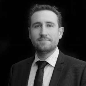 A man in a suit and tie poses for a formal portrait against a dark background.