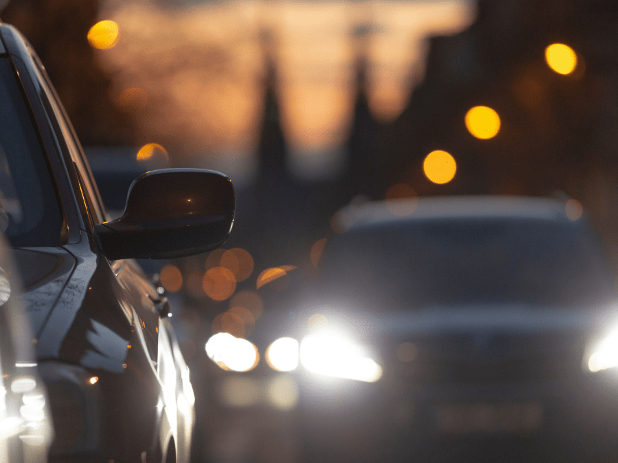 Cars on a road with headlights on, photographed at dusk with a shallow depth of field and blurred background lights.