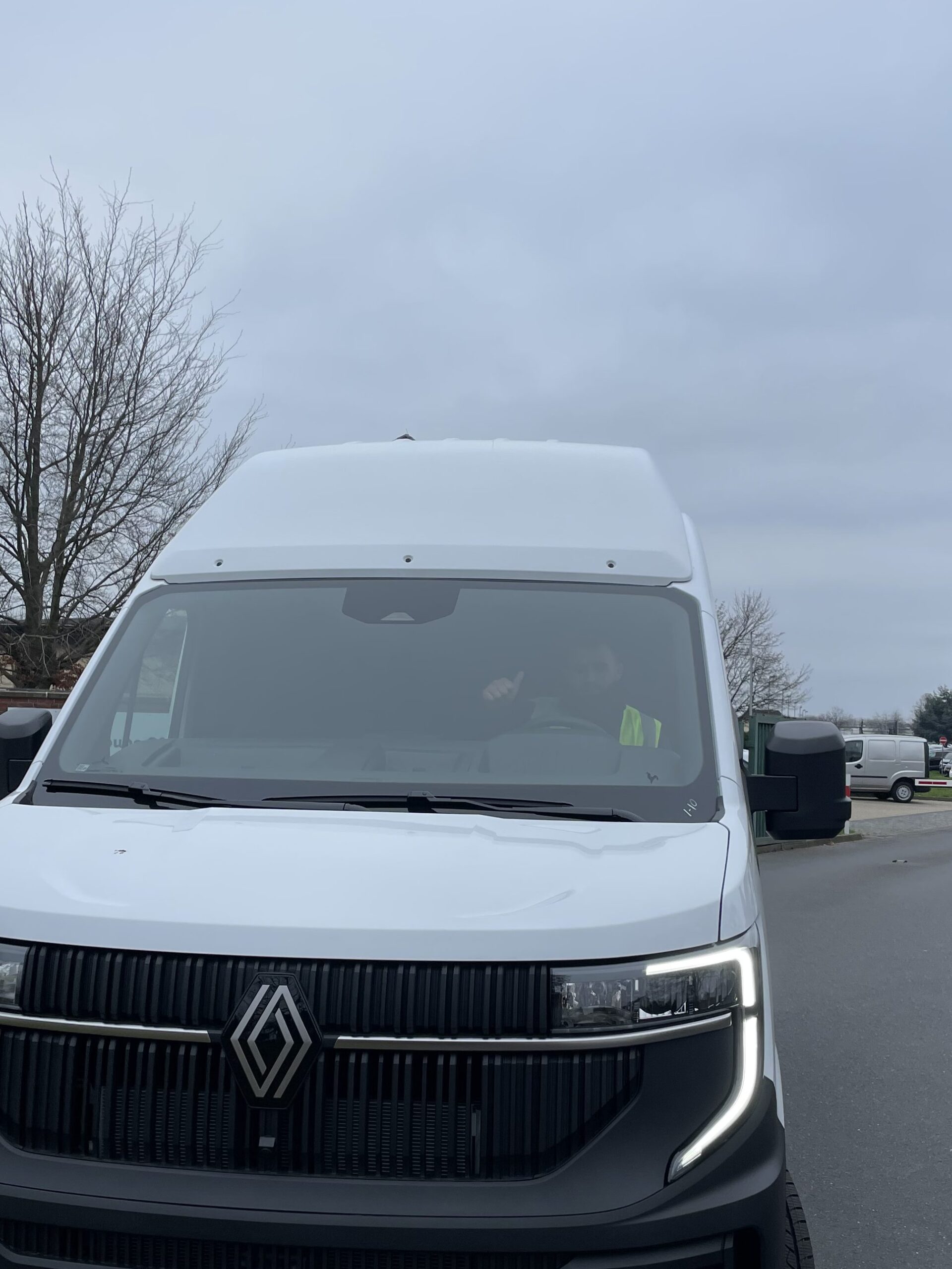 A white Renault van used for a Fallstudie SV-Transporte is parked on a street near a parking area on an overcast day, with some trees and buildings visible in the background.