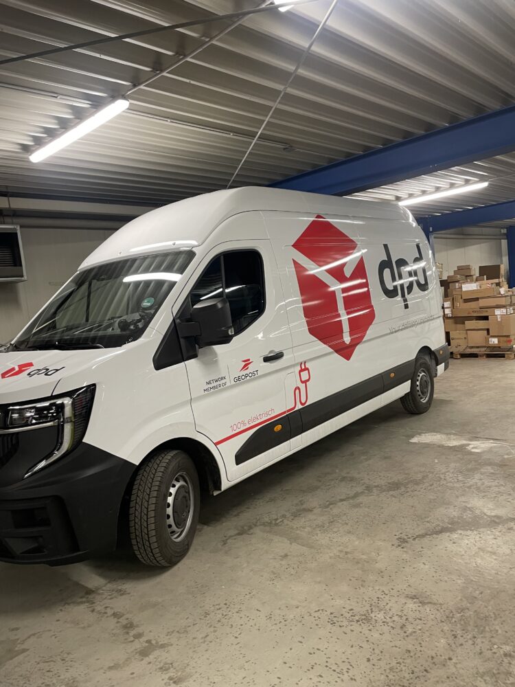 A white delivery van with red and black branding, part of a Fallstudie SV-Transporte, is parked indoors near stacked cardboard boxes.