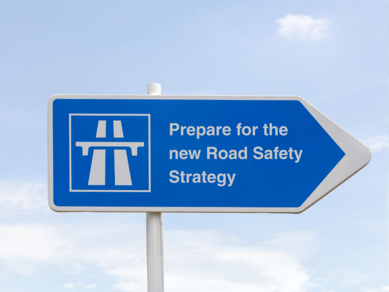 Blue road sign with a motorway symbol and the text "Prepare for the new Road Safety Strategy" against a blue sky background.