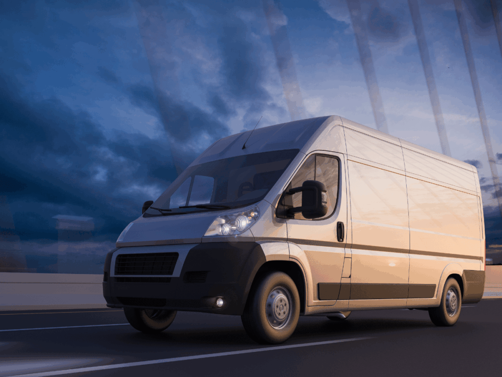 White cargo van driving on a motorway during dusk, with a cloudy sky and bridge cables visible in the background—a scene that underscores the importance of routine van safety checks before every journey.