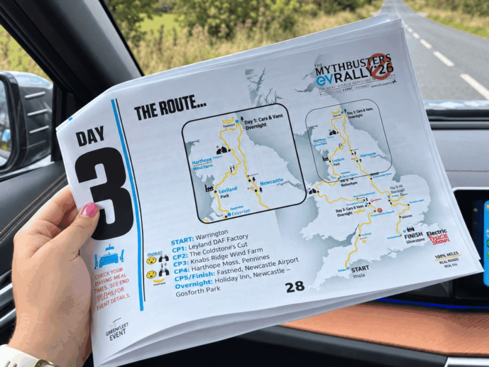 A person holds a printed route map for Day 3 of the EV Rally, showing checkpoints and stops across the UK, inside a car on a country lane.