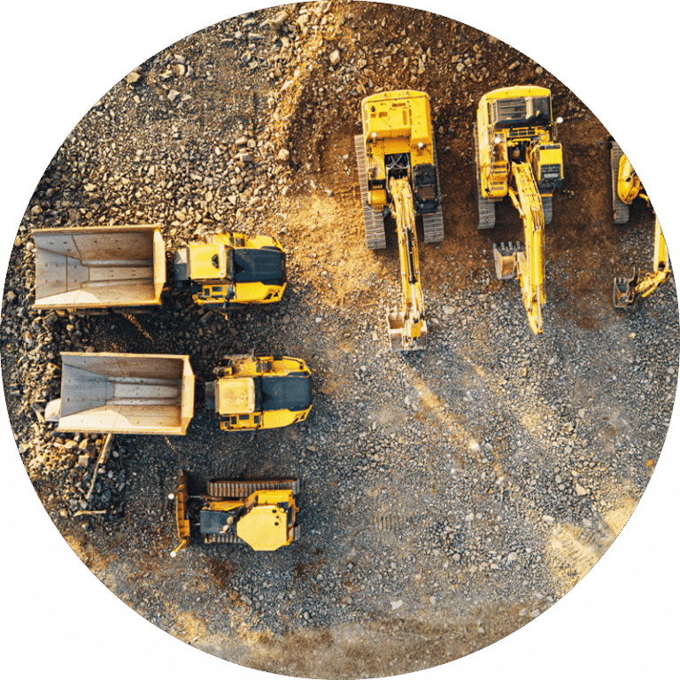 Aerial view of several yellow construction vehicles and dump trucks parked on a gravel site used for construction fleet tracking.