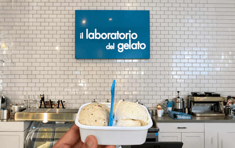 A hand holds two scoops of gelato in front of an “il laboratorio del gelato” sign, an area monitored by electric vehicle tracking.