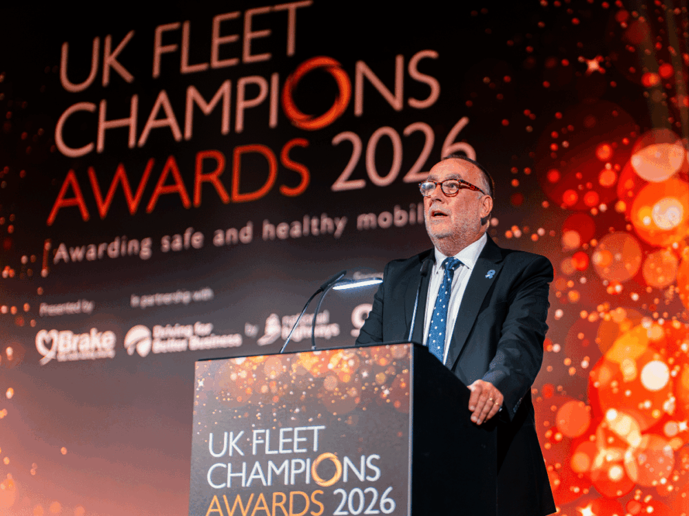 A man in a suit and glasses speaks at a lectern during the UK Fleet Champions Awards 2026.