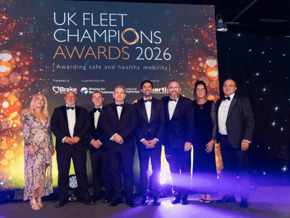 Eight people in formal attire standing on a stage in front of a “UK Fleet Champions Awards 2026” backdrop.