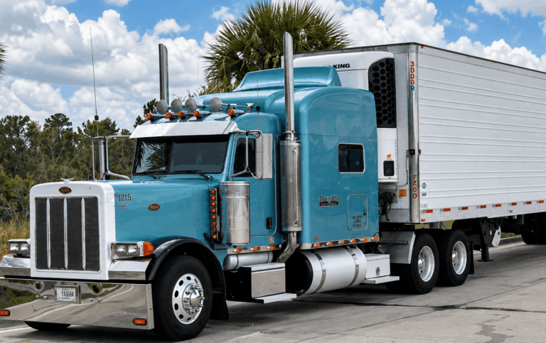 A light blue Peterbilt semi-truck pulling a white refrigerated trailer, monitored by electric vehicle tracking.